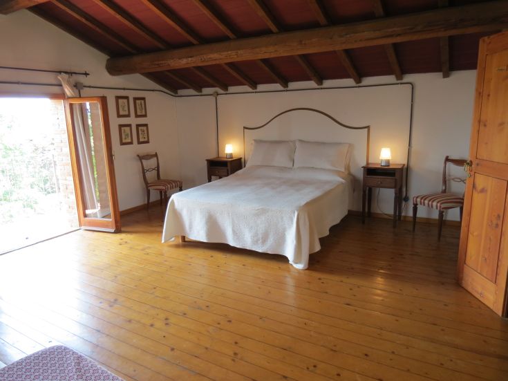 Gemütliches Zimmer mit einem Doppelbett, Holzboden und Fenstern mit Blick auf die Landschaft.