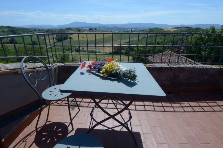 Ein Tisch mit Blumen auf einer Terrasse mit Blick auf sanfte Hügel und grüne Felder.