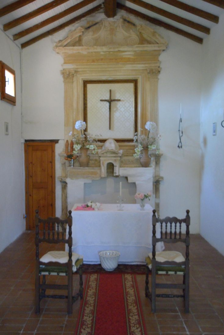 Innenraum eines historischen Palais mit einem einfachen Holzaltar und einigen Stühlen in einer ruhigen Umgebung.