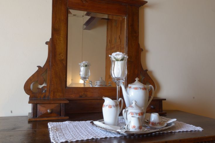 Teeservice auf einem Holztisch, mit einem großen dekorierten Spiegel, der die Umgebung spiegelt.