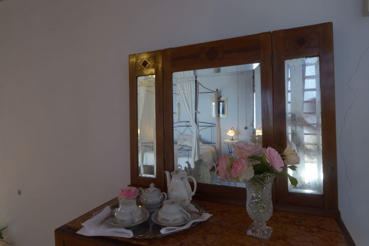 Ein Tisch mit einem Teeservice, Blumen und einem Spiegel. Die Atmosphäre ist einfach und einladend.