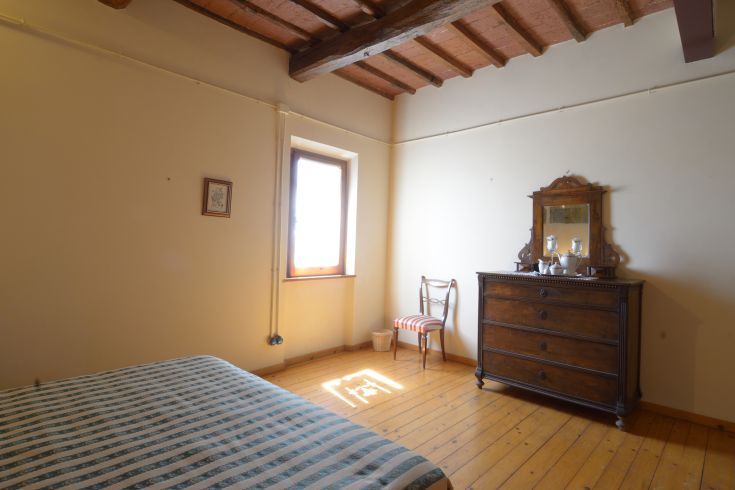 Ordentliches und gemütliches Schlafzimmer mit einem Bett, einer Vintage-Kommode und einem Fenster, das natürliches Licht hereinlässt.