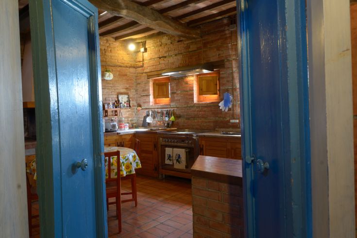 Eine einfache Küche aus Holz und Ziegeln, hell erleuchtet von Fenstern mit Blick auf eine grüne Fläche.