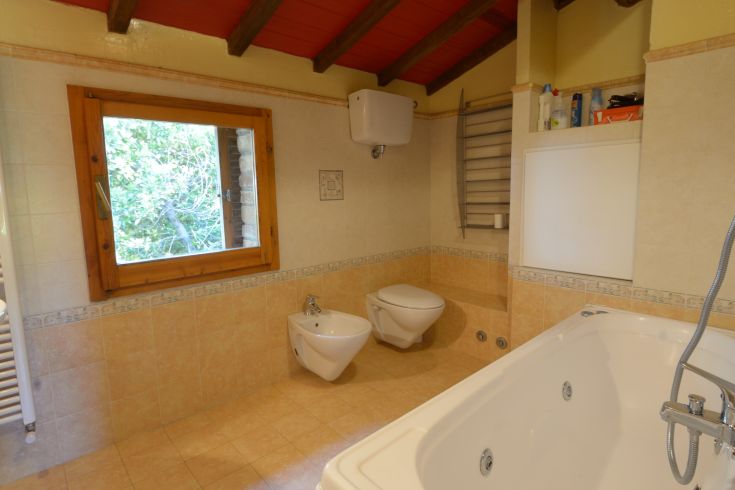 Ein geräumiges Badezimmer mit Badewanne, Sanitäranlagen und einem Fenster mit Blick auf eine grüne Landschaft.