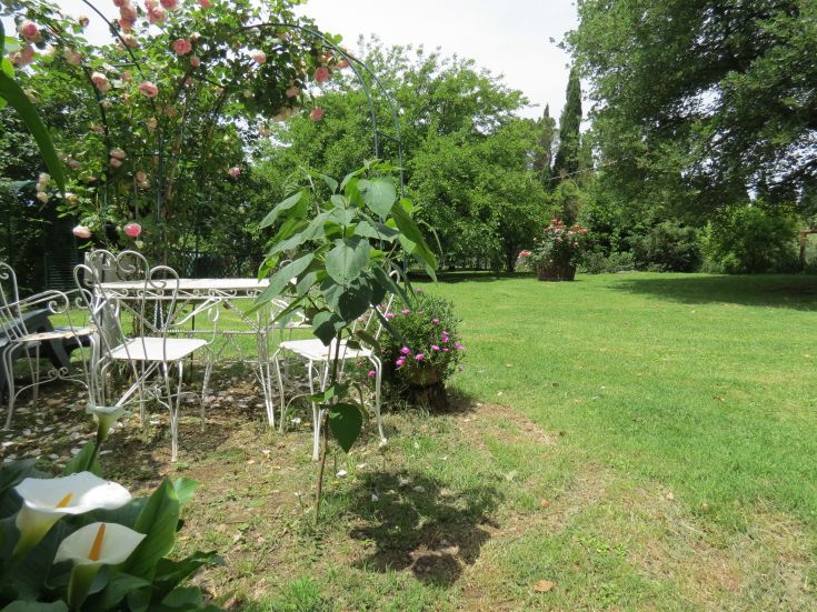 Ein Garten geschmückt mit Tisch und Stühlen, umgeben von Blumen und Bäumen. Eine friedliche Umgebung zum Entspannen.