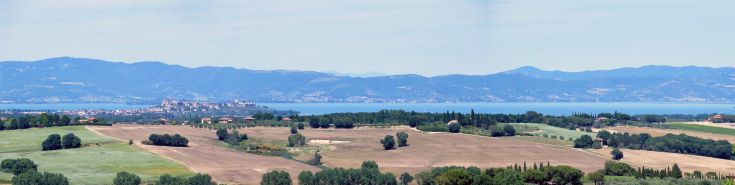 Panorama von Feldern und Hügeln mit einem See im Hintergrund, gelegen zwischen der Toskana und Umbrien.
