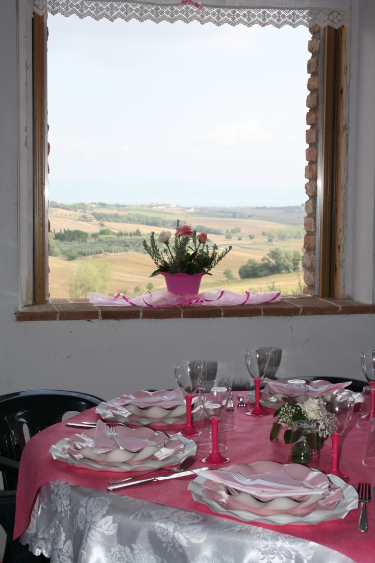 Dekorierter Tisch mit Tellern und Gläsern mit Blick auf eine hügelige Landschaft.