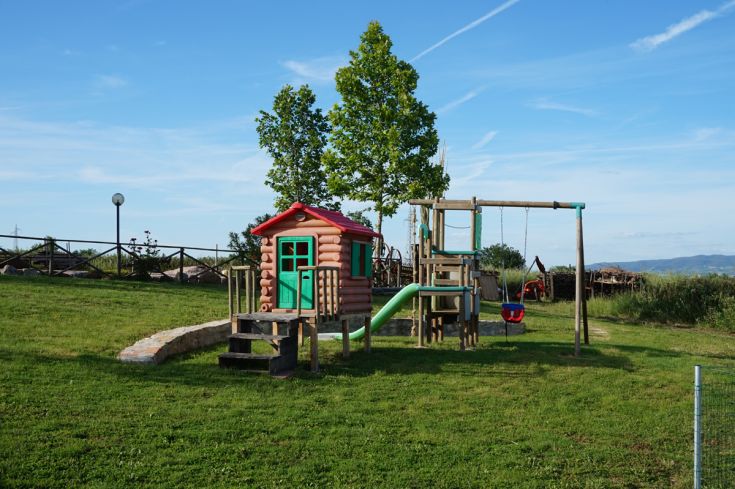 Area giochi per bambini con casetta in legno e altalena, immersa nel verde.
