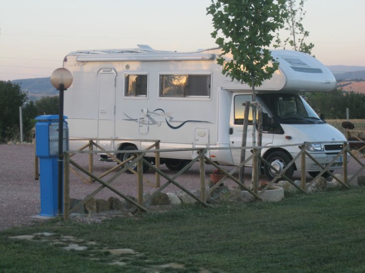 Un camper fermo in una zona serena circondata da aree verdi. L'ambiente è tranquillo e riposante.