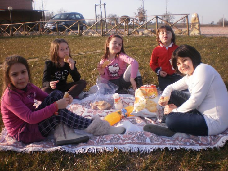 Un gruppo di ragazzi trascorre del tempo facendo un picnic all'aperto in un'area verde, tra sorrisi e stuzzichini.