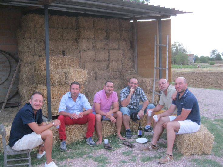 Un gruppo di amici si rilassa in un ambiente rurale, circondato da balle di fieno e alberi.