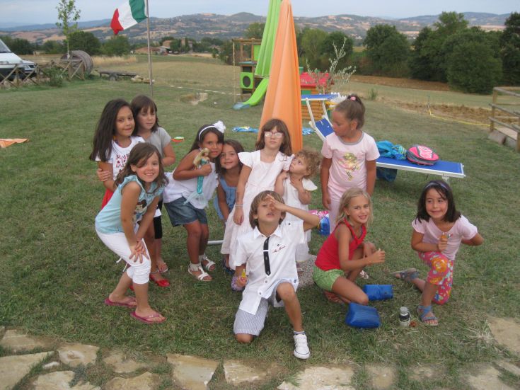 Un gruppo di bambini gioca sorridente in un'ambientazione naturale all'aperto.