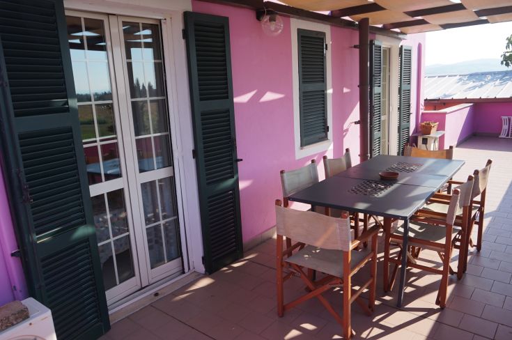 Spazio esterno sobrio con tavolo per sei, adornato da un muro color rosa.