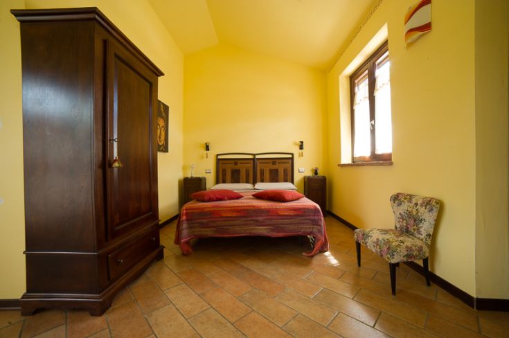 Camera in stile rustico, con pareti gialle e mobili in legno scuro, offre un ambiente luminoso e accogliente.