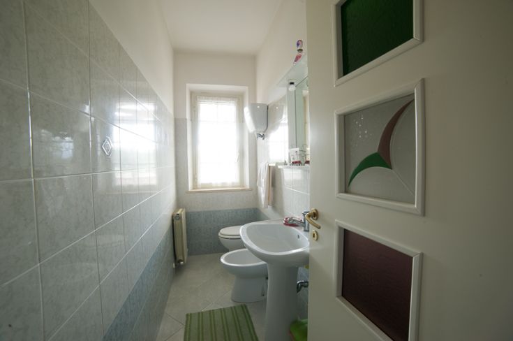 Bagno ben illuminato e ordinato con piastrelle chiare e una finestra che porta luce naturale.