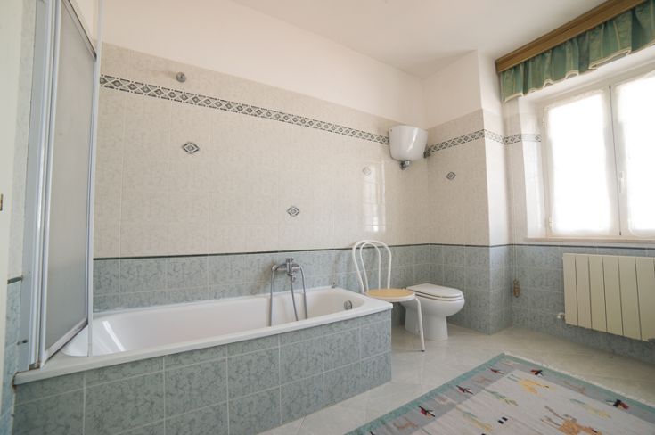 Bagno ben illuminato con vasca e piastrelle verdi, arredamento pratico e sobrio.