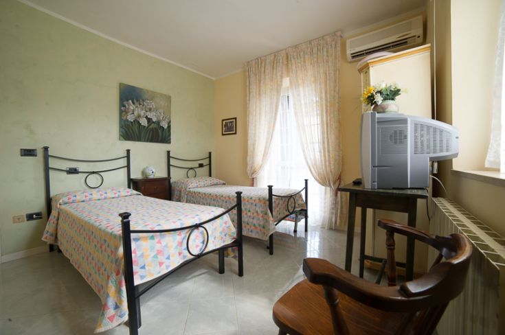 Camera semplice con letti separati, illuminata da una finestra che affaccia su una zona tranquilla.