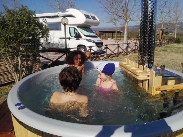 Tre bambini giocano in una vasca idromassaggio, circondati da un'area verde e alberi, immersi nella natura.