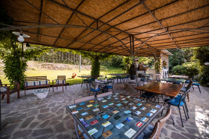 Area all'aperto con tavoli e sedie, circondata da alberi e piante tipiche della campagna umbra.