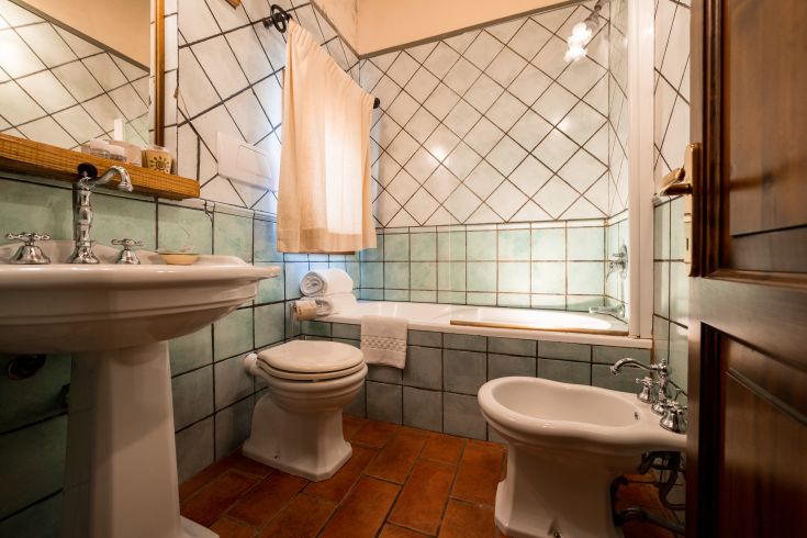 Bagno con piastrelle verdi e dettagli in terracotta, completo di vasca e illuminato da luce naturale.