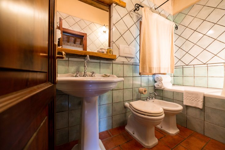 Bagno con piastrelle verdi e sanitari classici, illuminato dalla luce naturale, arredato con asciugamani morbidi.