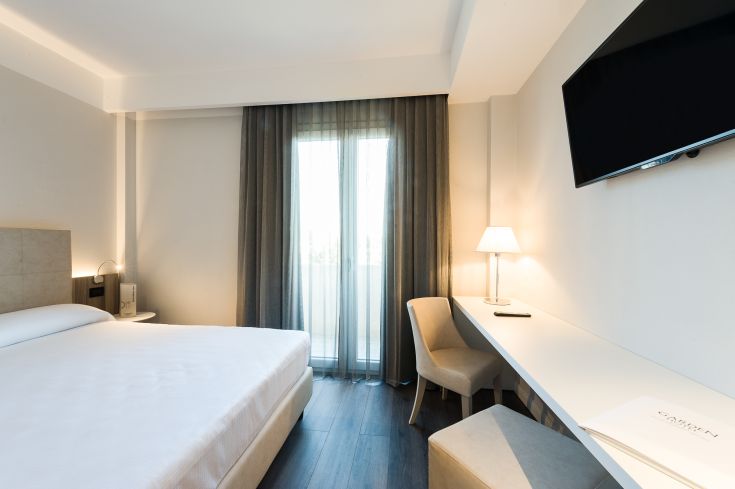 Camera semplice con letto matrimoniale, TV e scrivania. Illuminazione soft e panorama sul balcone.