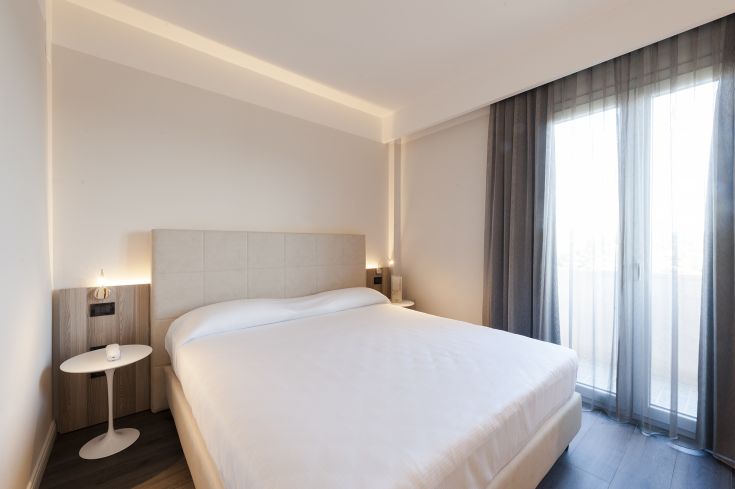 Camera semplice e luminosa con letto matrimoniale e panorama sulla città.