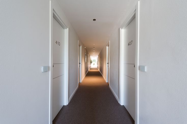 Corridoio di un palazzo con porte numerate, illuminato dalla luce naturale proveniente dalle finestre.