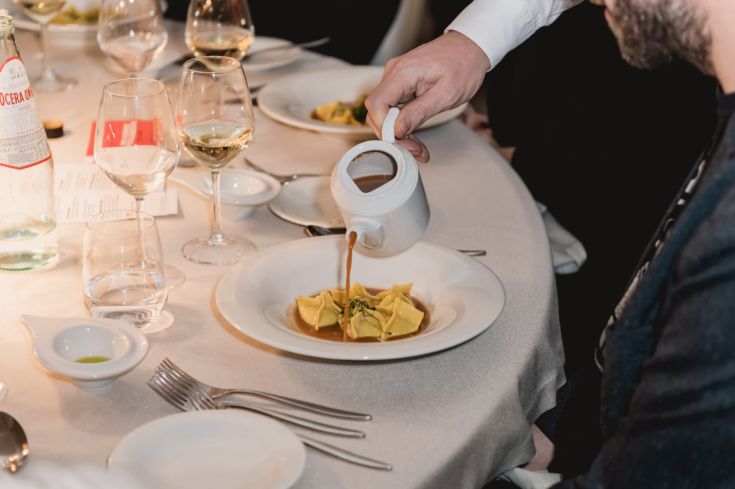 Un cameriere serve un brodo su un piatto di ravioli in un contesto raffinato.