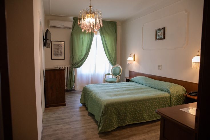 Camera spaziosa con arredi essenziali e luce naturale che filtra da un lucernario. Atmosfera rilassante e serena.