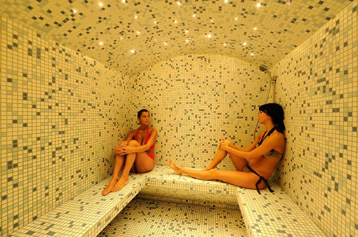 Due donne si rilassano in un centro benessere caratterizzato da piastrelle blu e bianche, un luogo tranquillo per il riposo.