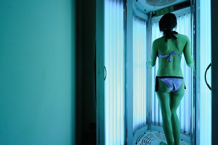 Una donna sdraiata su un lettino abbronzante, con luci blu che creano un'atmosfera luminosa.