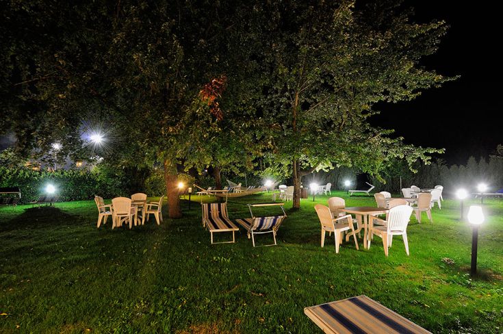 Un grande giardino adornato da luci delicate che creano un'atmosfera serena, completo di tavoli e sedie per il relax.