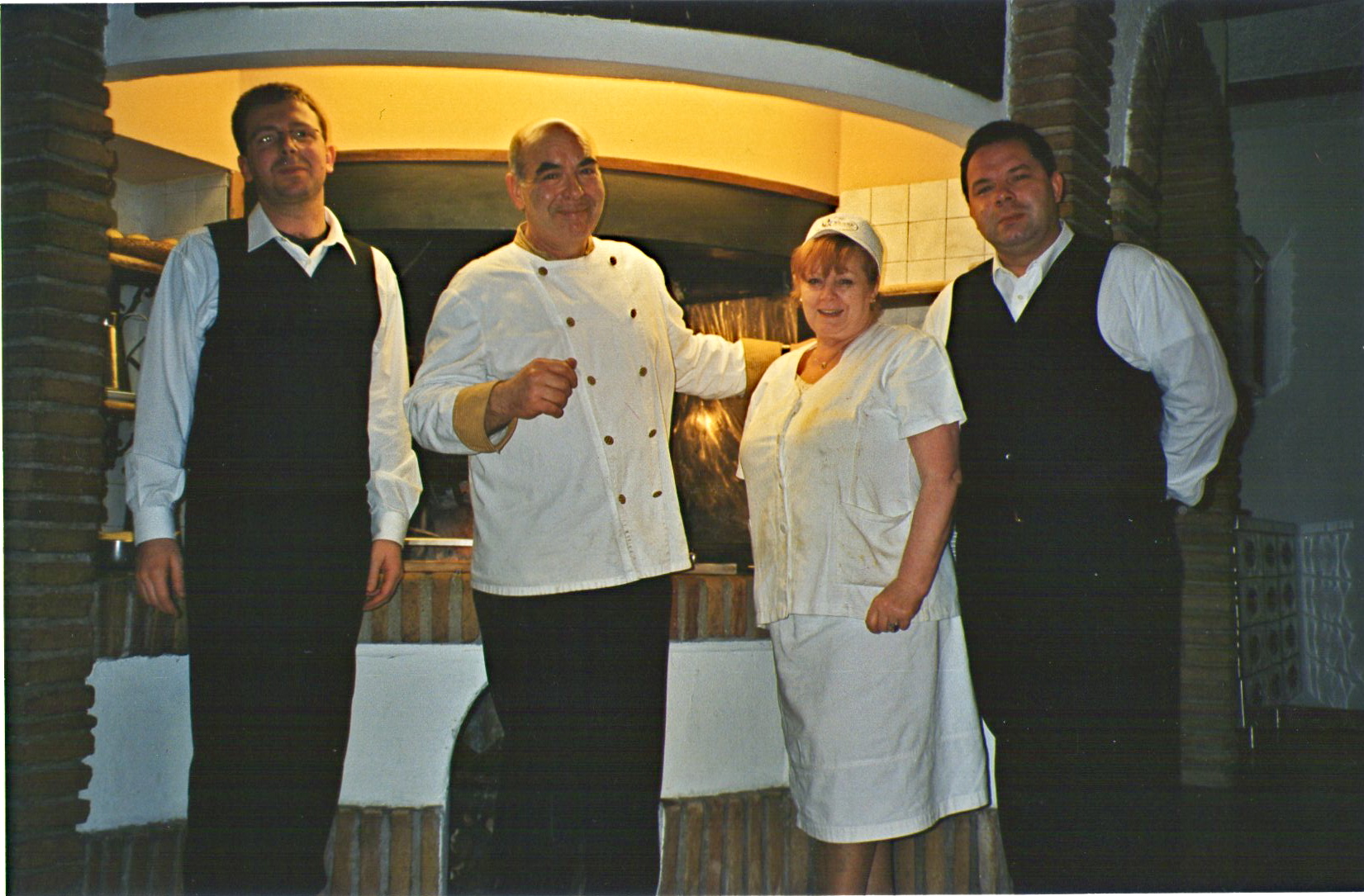 Un gruppo di persone sorridenti in abbigliamento da ristorante davanti a un camino. Atmosfera familiare.