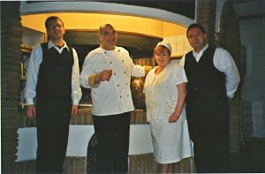 Un gruppo di persone sorridenti in abbigliamento da ristorante davanti a un camino. Atmosfera familiare.