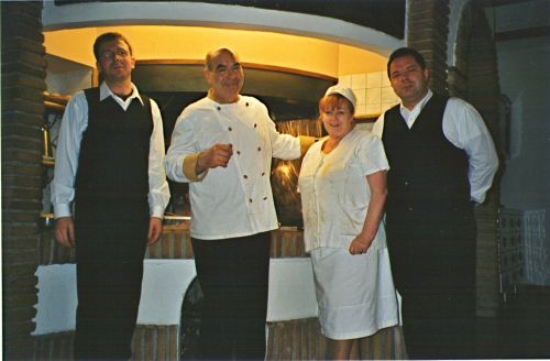 Eine Gruppe von lächelnden Restaurantmitarbeitern in Uniformen vor einem Kamin, der eine gemütliche, familiäre Atmosphäre schafft.