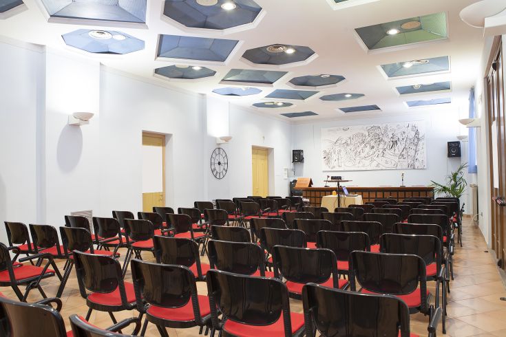 Ambiente contemporaneo e ben illuminato, adatto a riunioni o presentazioni, con posti a sedere disposti in modo ordinato. Elementi architettonici gradevoli.