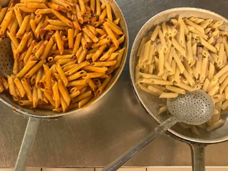 Due diverse tipologie di pasta, una con sugo di pomodoro e l'altra con un condimento cremoso, sono in cottura in due pentole.