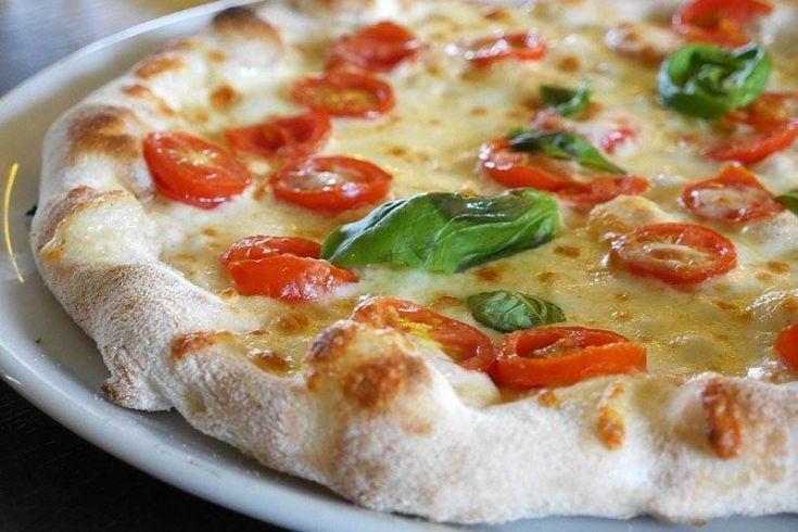 Una pizza margherita preparata con pomodoro fresco e foglie di basilico.