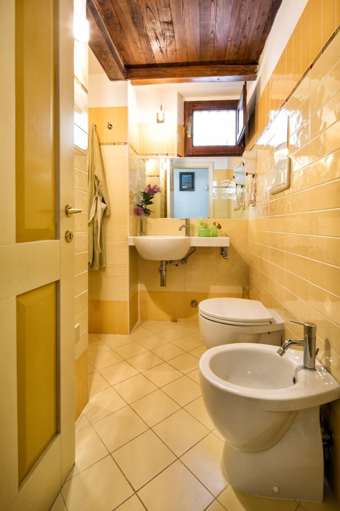 Bagno comodo con pareti gialle e soffitto in legno, arredato con elementi di design contemporaneo.