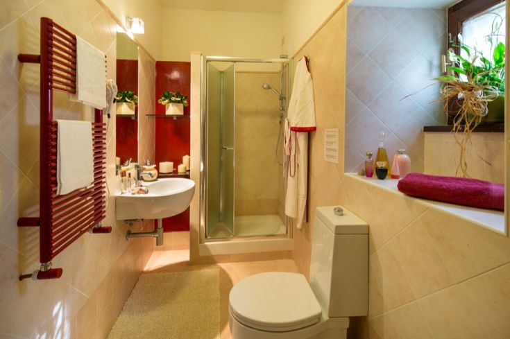 Bagno arredato con piastrelle chiare, una doccia funzionale e tocchi di colore rosso. Ambiente semplice e curato.