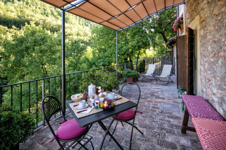 Colazione servita all'aperto su una terrazza immersa nel verde, con vista su un paesaggio naturale.