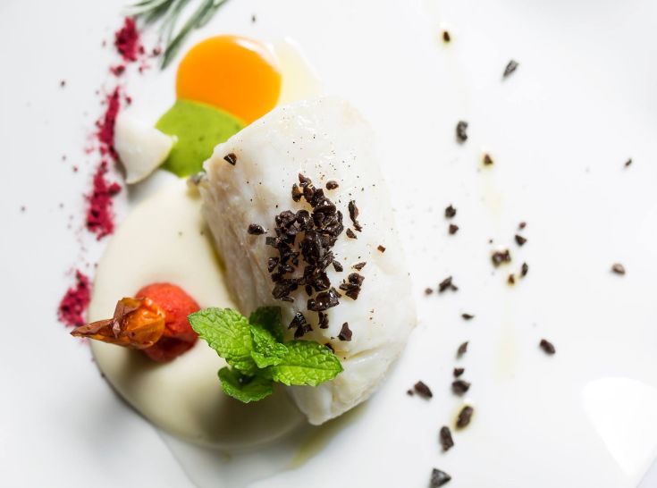 Un plat de poisson présenté avec des sauces et des décorations fraîches.