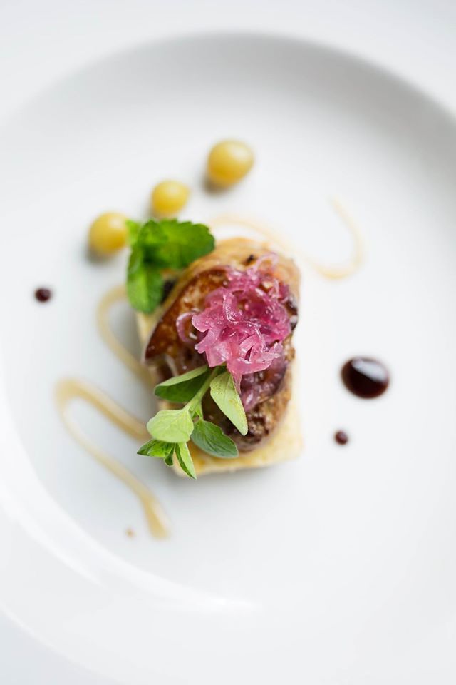 Une assiette décorée avec des herbes fraîches et des sauces, servie sur une simple assiette en céramique blanche.