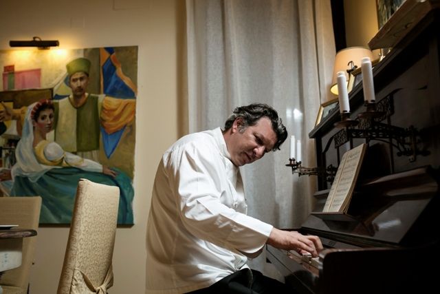 Un homme joue du piano dans une pièce élégante éclairée par des bougies, avec un tableau en arrière-plan.