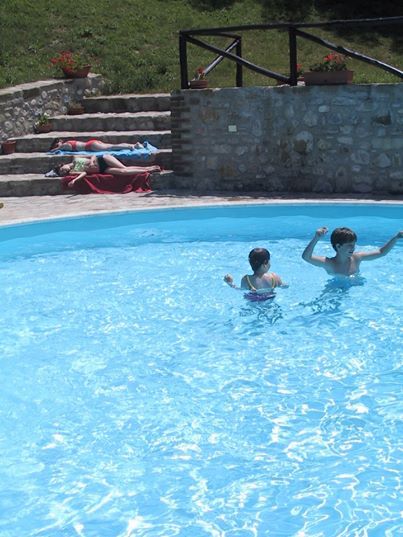 Due bambini giocano in piscina, mentre altre persone si godono il relax a bordo vasca.