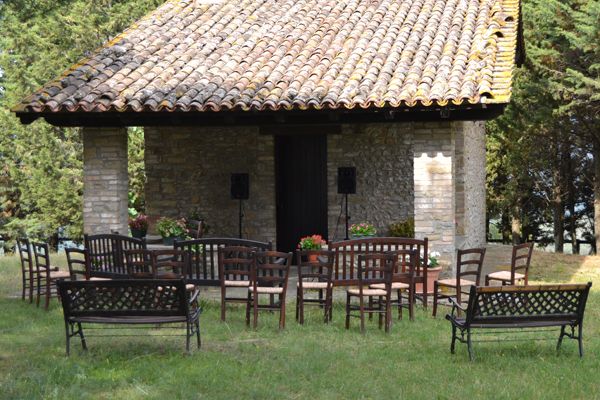 Un'area esterna con sedie disposte intorno a un edificio rustico, immerso nella vegetazione.