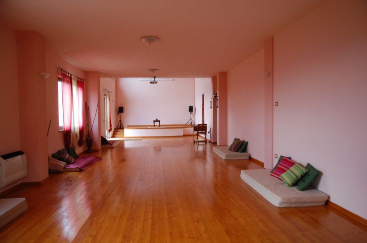 Ambiente sereno e ben illuminato, adatto per la meditazione, con tappeti e cuscini di varie tonalità.