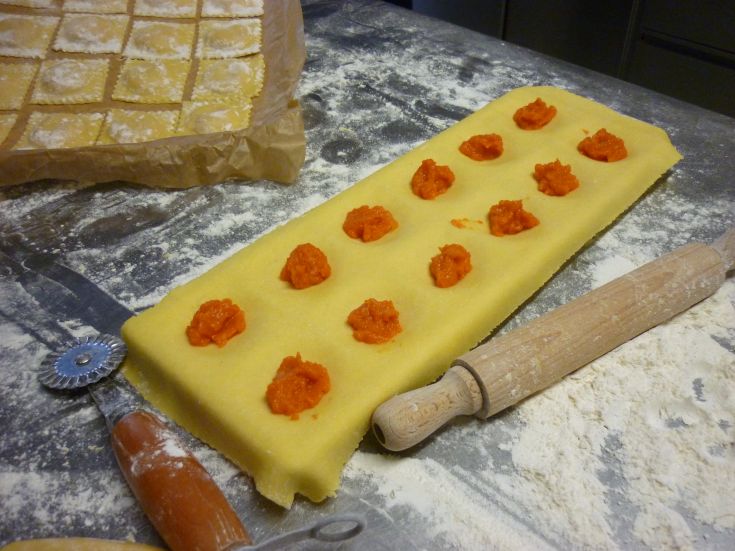 Preparazione di ravioli farciti con zucca su un tavolo di legno infarinato.