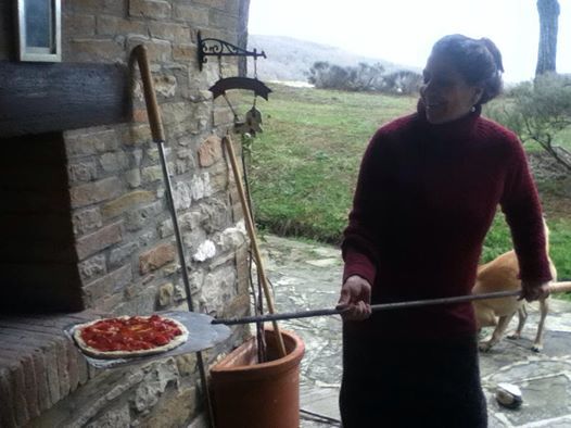 Una donna sforna una pizza in una cucina rustica con un panorama verde all'esterno.